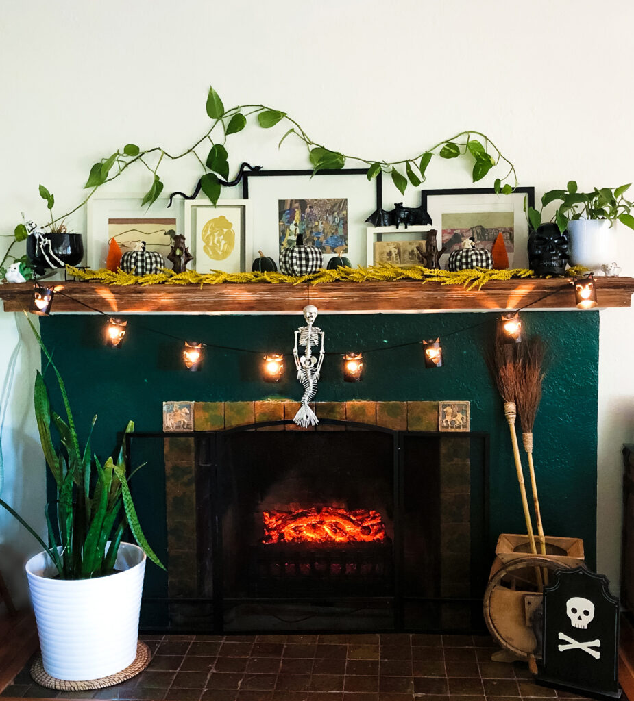 Fireplace decorated with halloween, large plant, broom stick, string lights, pitcures, skeleton mermaid in middle